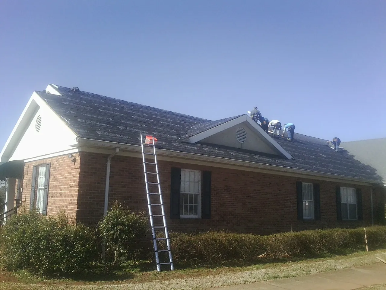 Crew tearing shingles off a brick ranch roof with a ladder set — Metal Roof Repair work by our crew in North East