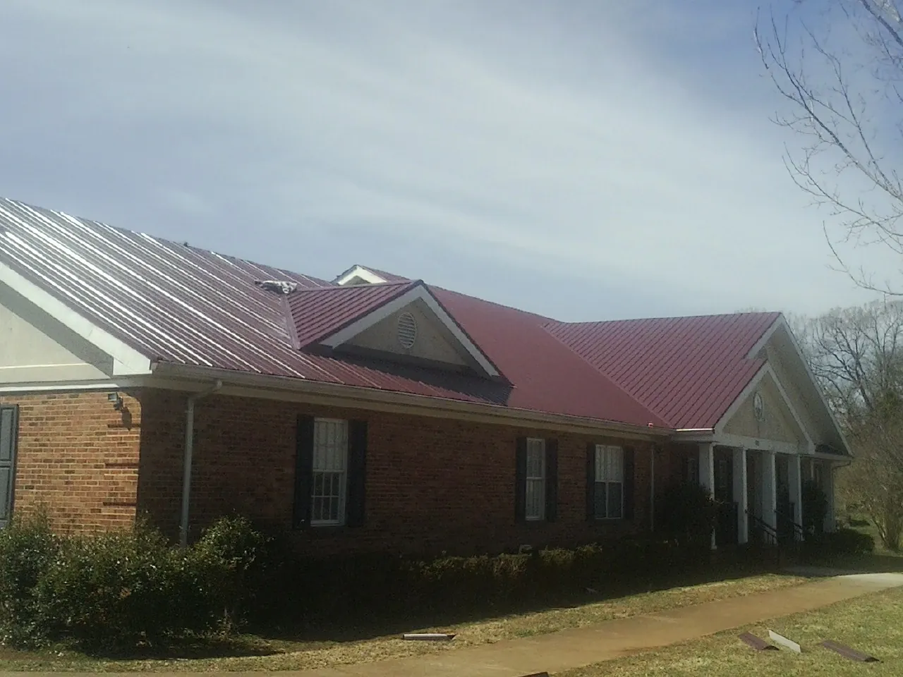 Red metal roof with gabled entries on a long brick building, from a Hail Damage Roof Repair job in North East